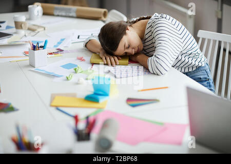 Vista laterale ritratto contemporaneo di giovane donna che dorme sul tavolo di lavoro , spazio di copia Foto Stock
