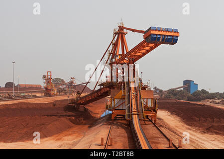 Operazioni portuali per la gestione e il trasporto di minerale di ferro. Parte posteriore della benna reclaimmer raccoglitore di minerale di bonifica sul trasportatore. Altri impilatori in distanza Foto Stock