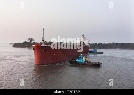 Operazioni portuali per la gestione e il trasporto di minerale di ferro. Rimorchiatori di manovra e girando il trasbordo nave prima di docking e di carico di minerale fino al molo Foto Stock