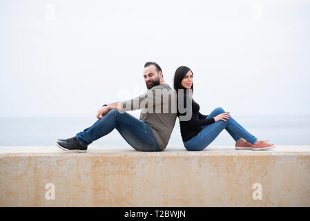 Me e donna seduta di schiena sulla spiaggia Foto Stock