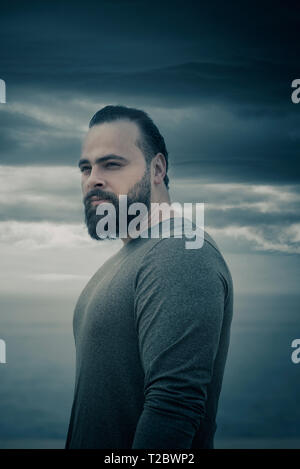 Malinconici uomo barbuto che guarda lontano all'aperto Foto Stock