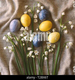 Fiori di Primavera sono bucaneve e uova di Pasqua decorate in giallo e blu di colori su una tela morbida. Set di festa. Biglietto di auguri. Foto Stock