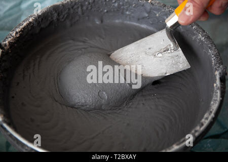 Mano del lavoratore con una cazzuola in una benna con intonaco di calcestruzzo Foto Stock