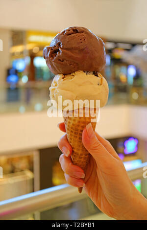 L'immagine verticale della mano che tiene cono gelato con due palline di cioccolato e burro di arachidi ice Foto Stock