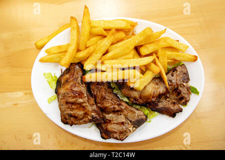 Grigliata di costolette di agnello con patate fritte su una piastra su un tavolo di legno. Il cibo Foto Stock