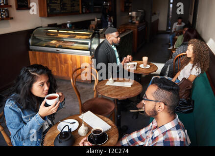 Varie Gruppo di giovani seduti ai tavoli in una caffetteria alla moda di bere il caffè e parlare insieme Foto Stock