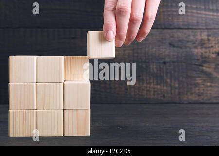 Donna mettendo a mano il pezzo finale del cubo di legno in posizione - Realizzazione concetto. Terminare il concetto del progetto Foto Stock