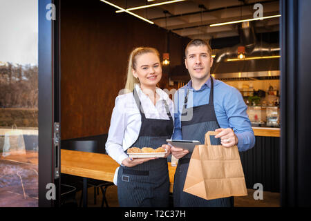 I proprietari di piccole imprese in piedi all'ingresso del ristorante alla moda di consegnare gli ordini da asporto Foto Stock