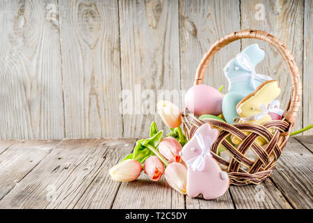 Vacanze di Pasqua saluti sfondo, cesto con colori pastello e uova di Pasqua tortina di cottura i cookie, fiori di primavera. Rustico in legno sfondo, copia sp Foto Stock