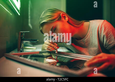 La vita o la tossicodipendenza. Addict la decisione. Giovane tossicodipendente con laminati banconota si siede in una posa per lo sniffing di cocaina in casa di farmaco il wc. N. di Foto Stock