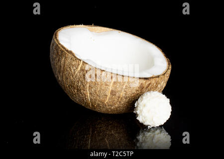 Una metà di carni bio noce di cocco con una piccola sfera di cacao isolato sul vetro nero Foto Stock