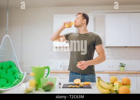 Giovane uomo bello bere il succo d'arancia fresco in cucina. Cibo sano. Pasto vegetariano. La dieta detox Foto Stock