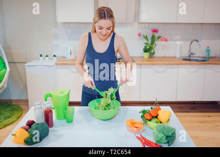 Vegan sorridente donna bionda Delizie insalata in cucina. Cibo vegetariano. Mangiare sano. Dieta vegana Foto Stock