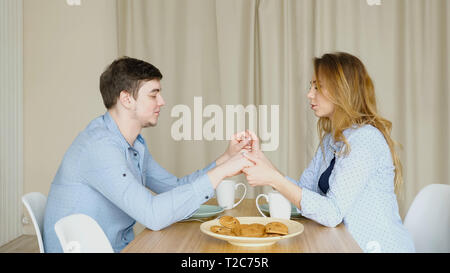 Ragazza bionda e guy siedono al tavolo di fronte a ogni altra mano nella mano e pregare prima di avere la prima colazione contro la tenda