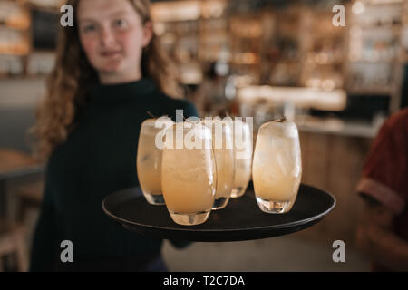 Ritratto di un giovane sorridente cameriera portando un vassoio di bevande mentre si lavora in un bar di sera Foto Stock