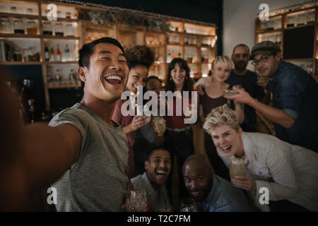 Diversi gruppi di giovani amici di ridere e di parlare insieme selfies durante una notte di divertimento in un bar Foto Stock