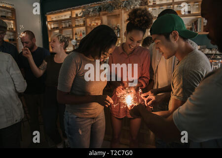 Gruppo di diversi giovani amici botti di illuminazione mentre avente una serata divertente insieme in un bar alla moda Foto Stock