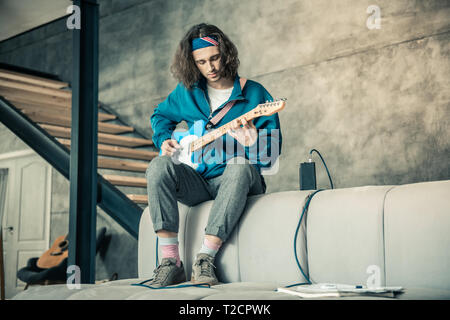 Focalizzato attento ragazzo in variopinti bandana sperimentando con la sua chitarra Foto Stock