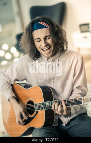 Con i capelli lunghi bello artista rumorosamente a cantare e suonare la chitarra Foto Stock