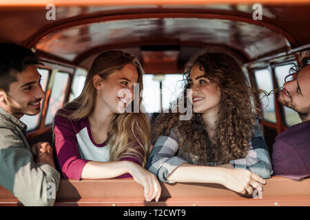 Un gruppo di giovani allegri amici con un minivan retrò su roadtrip attraverso la campagna, seduti in un'auto. Foto Stock