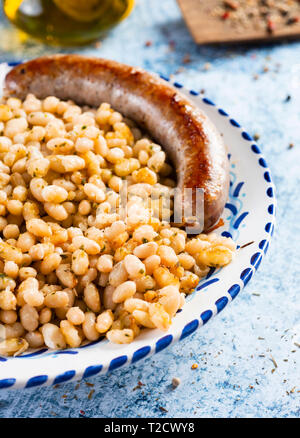 Botifarra amb mongetes fritto di fagioli bianchi e salumi tipici della Catalogna, Spagna, servita in un piatto di portata in ceramica bianca con un bordo blu, collocato su un marbl Foto Stock
