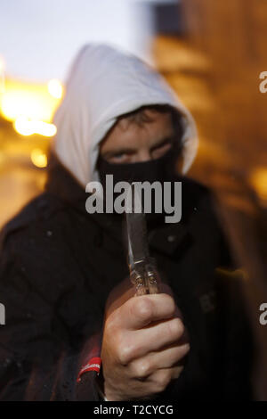 Il crimine di coltello. Uomo incappucciato brandendo un coltello butterfly Foto Stock