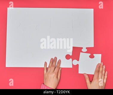 Femmina mette mano bianco grande puzzle su uno sfondo rosa, un elemento mancante, vista dall'alto Foto Stock