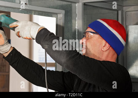 Valutazione esecutore esegue la costruzione e la fabbricazione di strutture metalliche. L'uomo bianco funziona con metallo in occhiali di protezione e guanti. Foto Stock