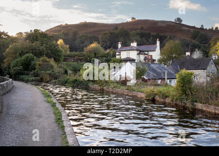 Welsh villaggio con case bianche e colline in lontananza, sera sun riflette sul canale Foto Stock