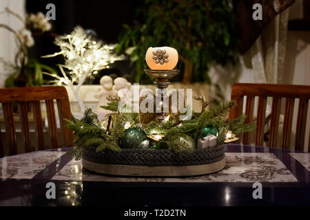 Una disposizione con candela e verde abete rami decora una stanza al tempo di Natale. Arredi di legno scuro e di una finestra con gli angeli di gesso e illumina Foto Stock