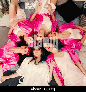 Sovraccarico di attraente ragazze giovani in rosa accappatoi sdraiato sul letto in cerchio. Addio al nubilato di partito. Foto Stock