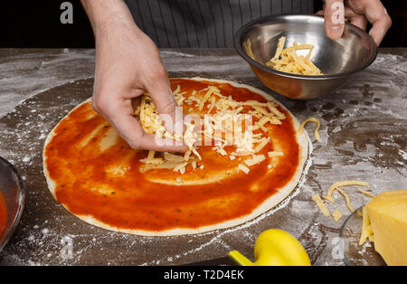 Cucina Italiana. Cuocere aggiungendo il formaggio grattugiato per la pizza in pizzeria Foto Stock