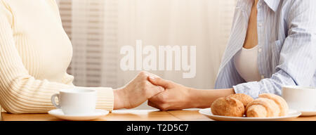 Figlia di madre tenendo la mano, mostrando la sua cura e supporto, avente la colazione a casa Foto Stock