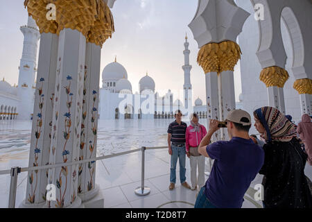 I turisti a scattare foto al Sheikh Zayed grande moschea cortile interno con ornati a tema floreale mosaici pavimentali, Abu Dhabi, Emirati Arabi Uniti Foto Stock