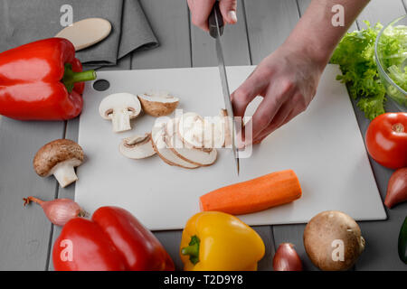 Uomo di taglio di funghi champignon a fettine su una lavagna bianca. La preparazione di verdure, cucina salutare. Foto Stock