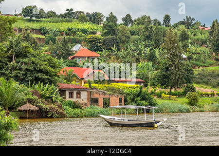 Tetto barca ancorata al litorale con villaggio ruandese in background, lago Kivu, Ruanda Foto Stock