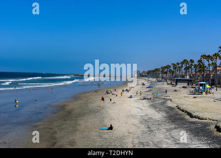 Affacciato su spiagge di sabbia con le persone e le palme e il blu del mare con onde di avvolgimento sul litorale sotto il luminoso cielo blu. Foto Stock
