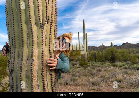 Bionda donna adulta abbraccia una grande cactus Saguaro in Arizona Deserto Sonoran Foto Stock