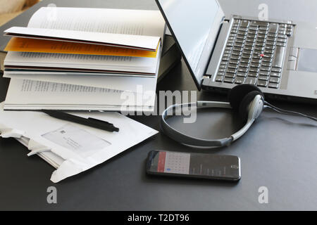 Computer portatile sul tavolo di lavoro con i libri, carte, matita, cuffie e lo smartphone Foto Stock