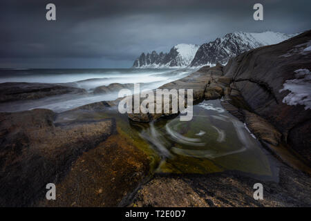 Tugeneset costa rocciosa con le montagne sullo sfondo in tempo nuvoloso, Norvegia Foto Stock