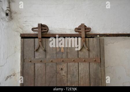 Fienile porta laterale cerniere su vecchio legno invecchiato porta che le diapositive a sinistra e a destra sono installate su una versione più recente edificio Foto Stock