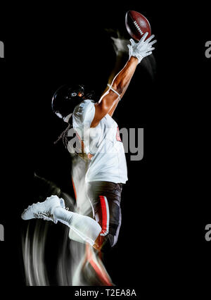 Uno african american football player uomo studio shot isolato su sfondo nero con luce pittura con movimento sfocato effetto di velocità Foto Stock