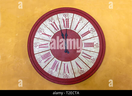 L'orologio rosso con numeri romani mostra per cinque minuti di dodici ore. La mezzanotte sulla torre con orologio sulla facciata di colore giallo. Foto Stock