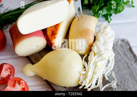 Un assortimento di dolci formaggi in varie forme e dimensioni su sfondo di legno, suluguni, spiralina, Cacocavallo con pomodori e basilico Foto Stock