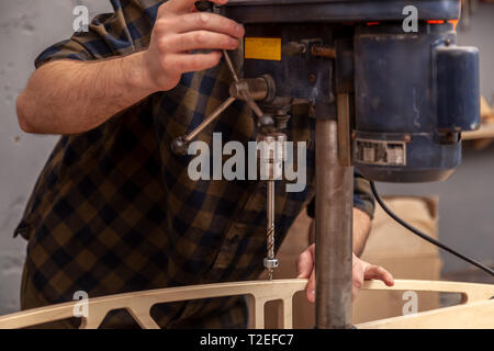 Chiusura del falegname esperto in abiti da lavoro e piccole buiness proprietario carving è una tavola di legno su un moderno trapano a mano in un workshop di luce sid Foto Stock