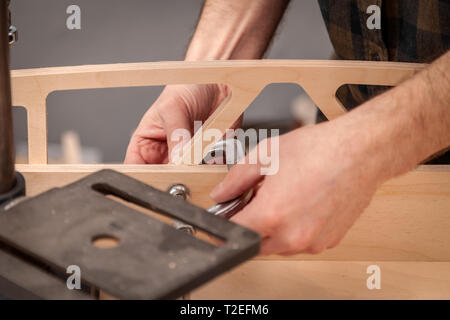 Riparazione della casa concetti, vicino. Falegnameria Artigianale. Cabinet-maker mani serra i dadi sul pannello di legno con un morsetto sul tavolo di lavoro in Foto Stock