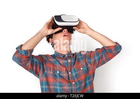 Ragazzo adolescente che indossa la realtà virtuale cuffie studio isolato in piedi sul muro bianco wathcing impressionato video Foto Stock