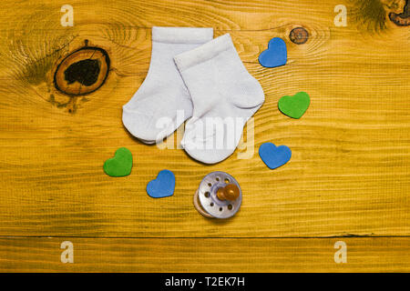 Little blue baby boy calze con succhietto e forme di cuore sul tavolo in legno.Baby annuncio concetto.tonica foto. Foto Stock