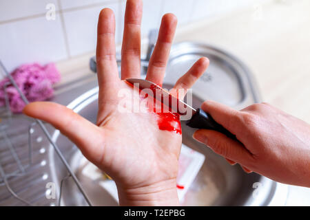 Una donna taglia stessa con un coltello da cucina Foto Stock