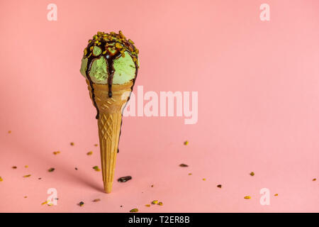 Strano concetto creativo instabile con pistacchio cono gelato con salsa di cioccolato e noci era cosparsa su sfondo rosa Foto Stock